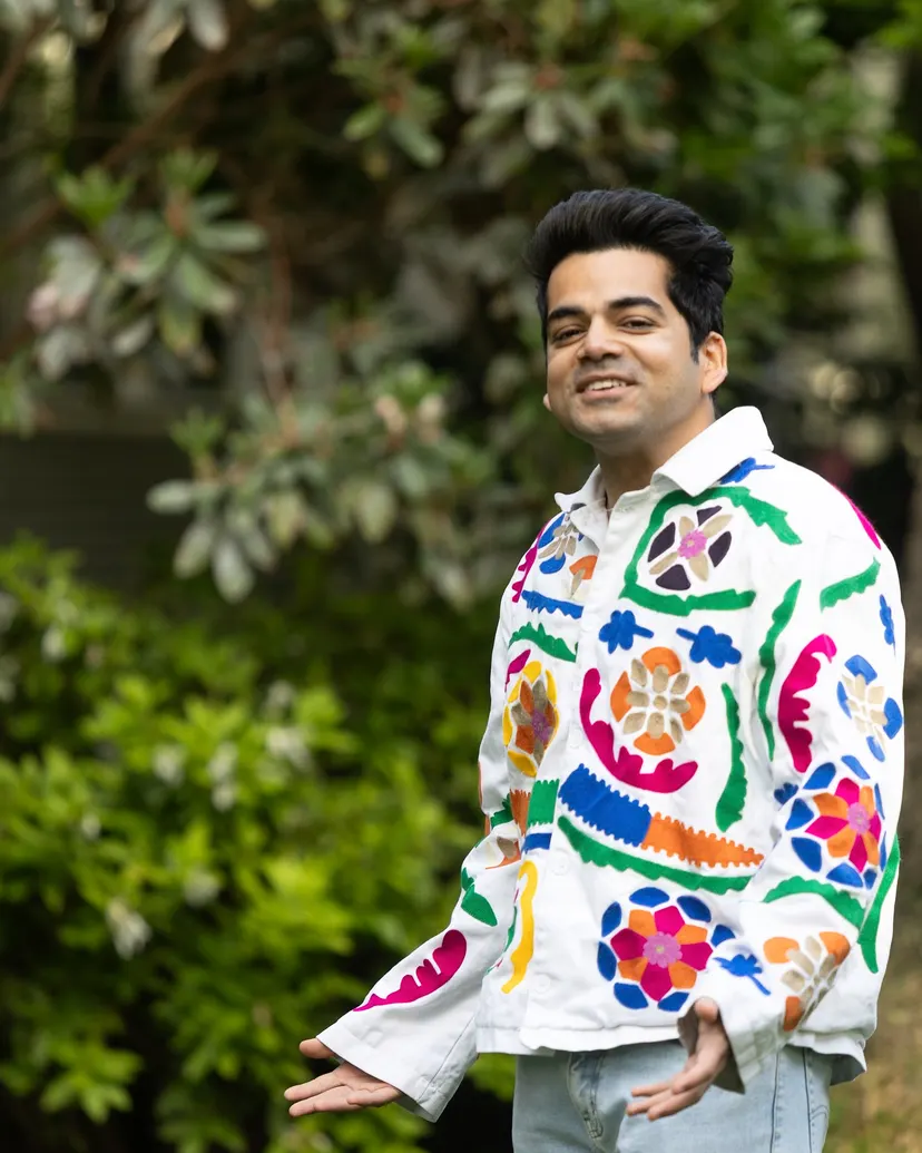 Kush in a white jacket embroidered with bright flowers, standing in a garden