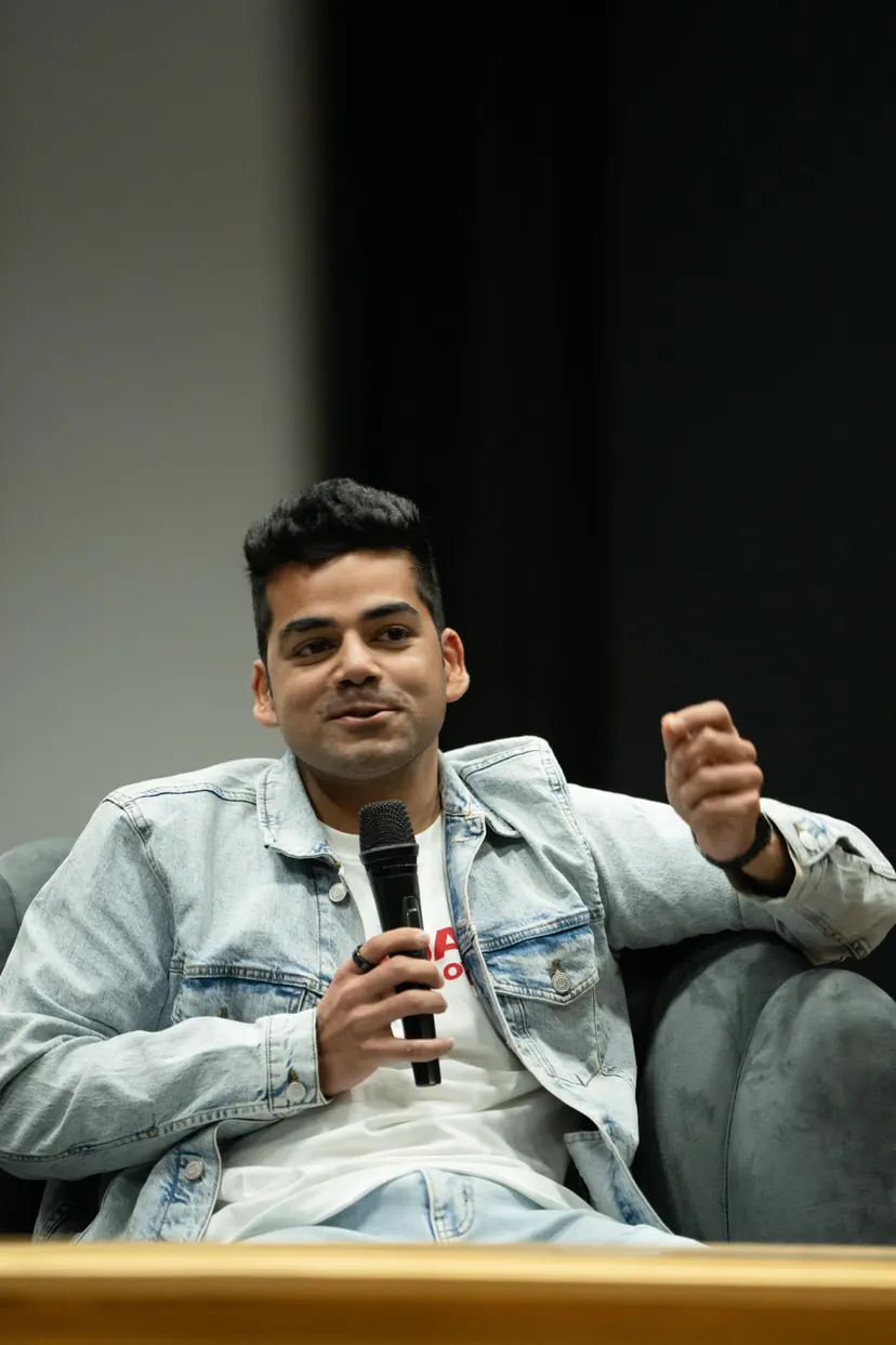 Kush in a denim jacket, speaking into a microphone on a stage