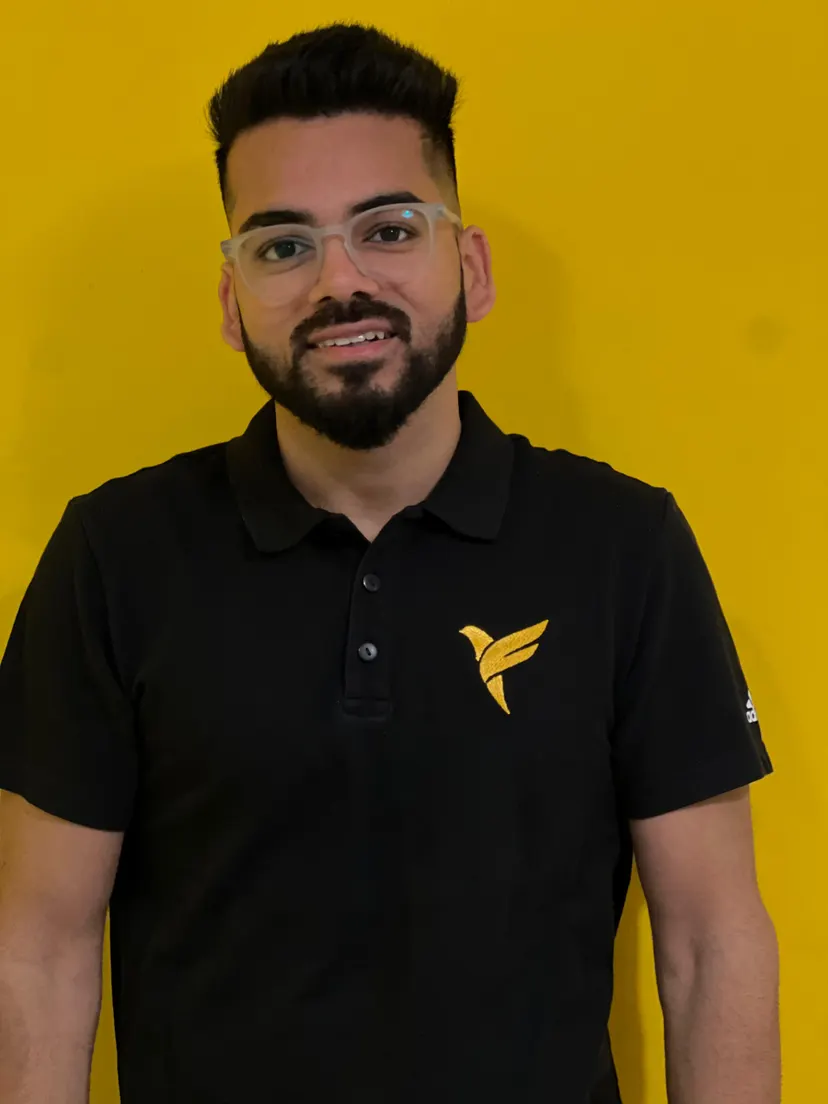 Kush in a black polo with a yellow logo, against a yellow wall